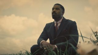 Michael B. Jordan dressed in a suit sitting in a field in Sinners