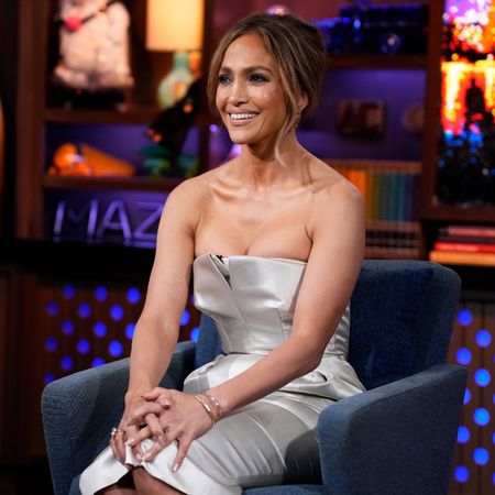 a woman sitting on a talk show set wearing a metallic silver dress