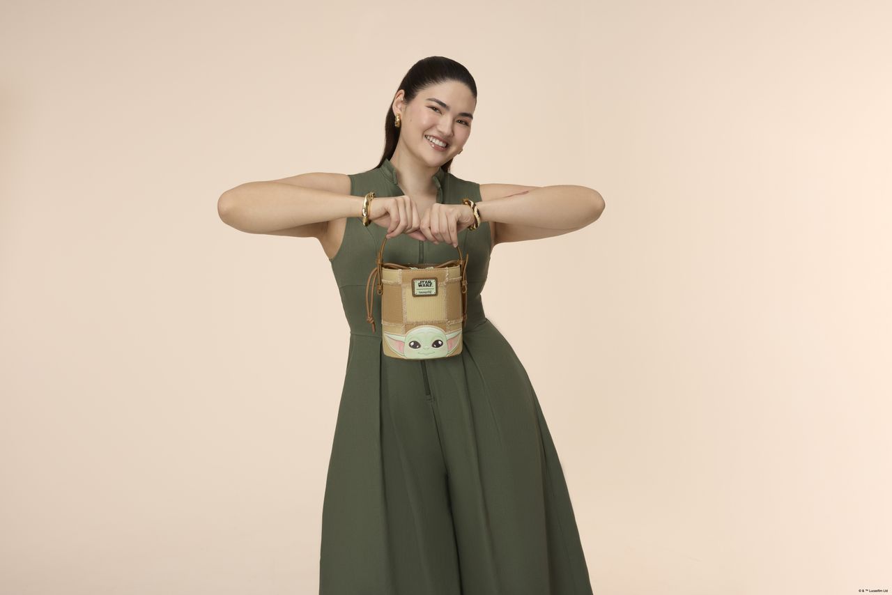 A woman holding a Loungefly bucket crossbody bag in a pink environment