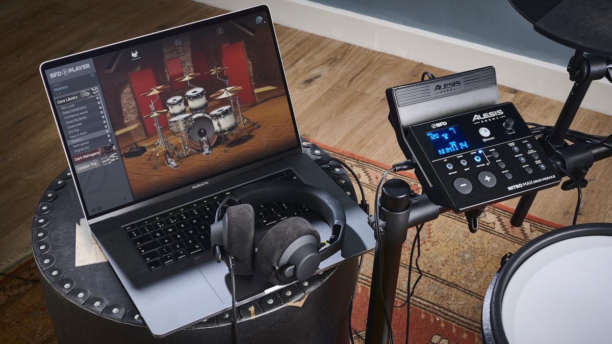Pair of headphones sat on a laptop next to an electronic drum set