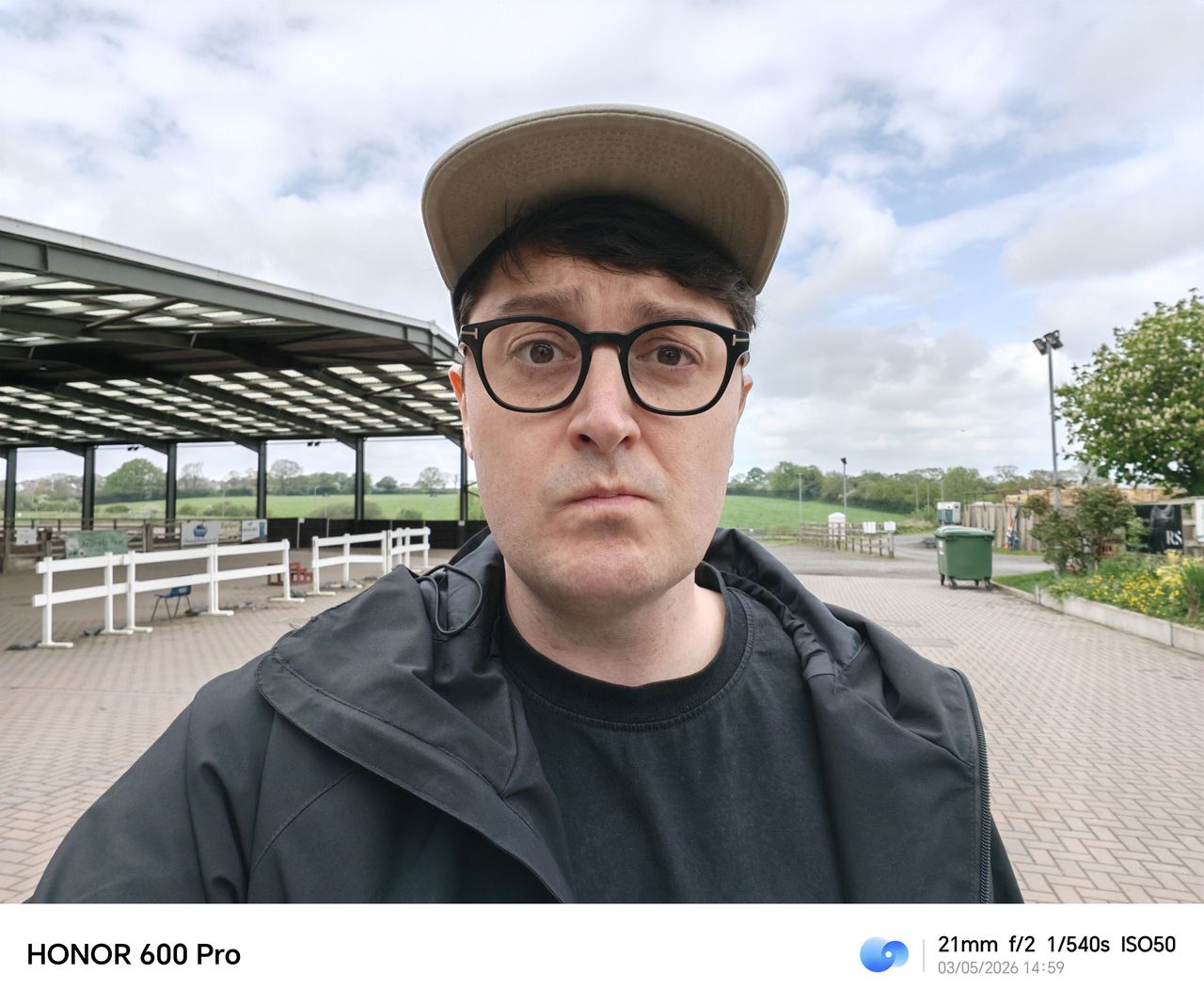 Wide-angle portrait selfie at an outdoor sports ground under a cloudy sky