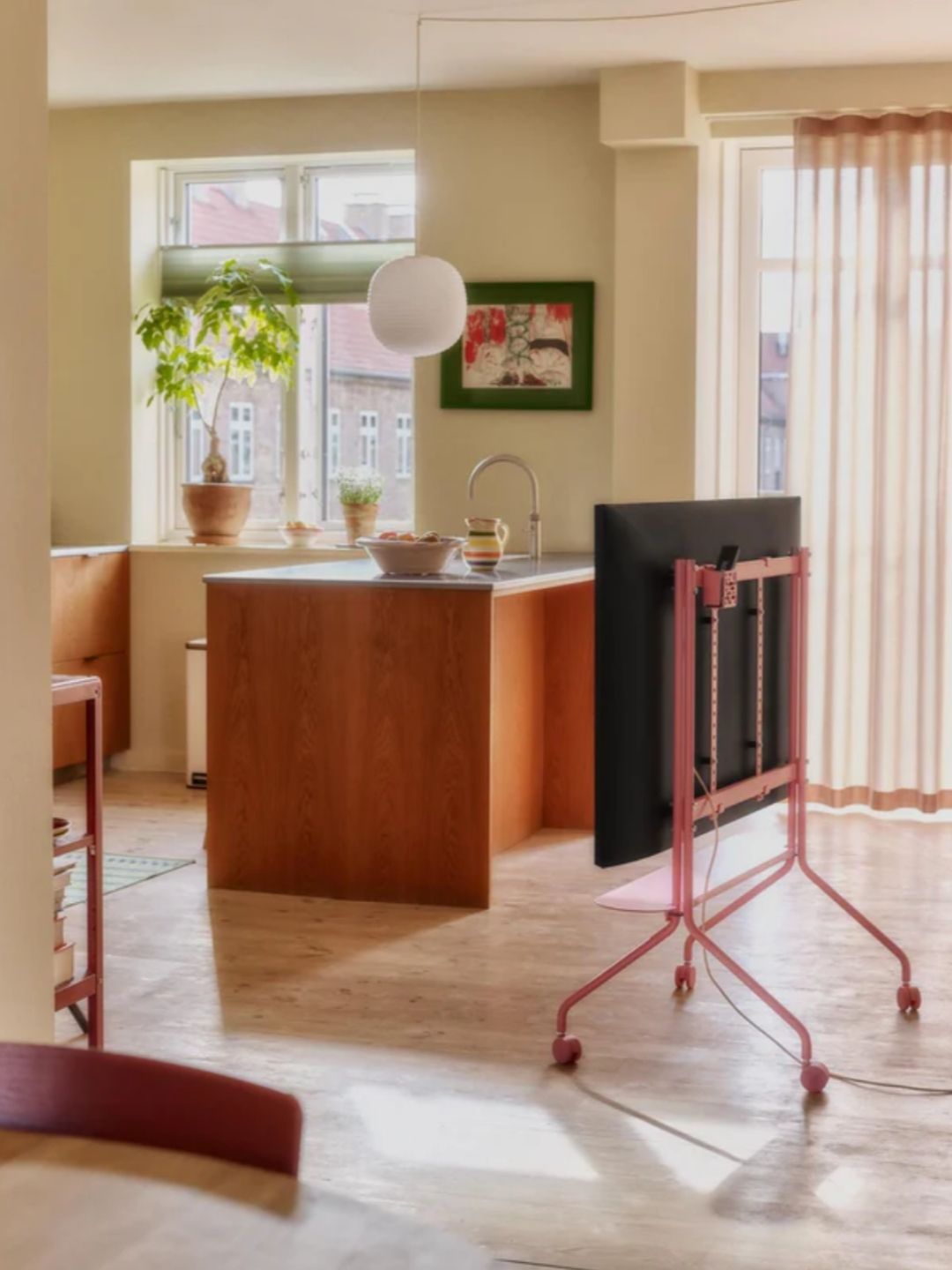 Image of a modern kitchen with a wooden island with a metal countertop. There is also a pink rolling TV stand.