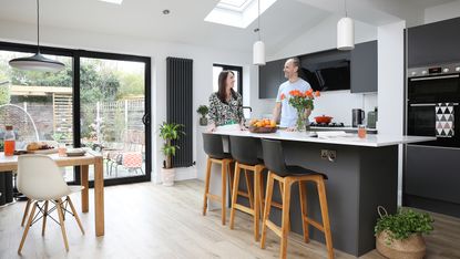 Extended kitchen-diner with black kitchen and island, white worktops, wood bar stools, sliding doors and wood dining table