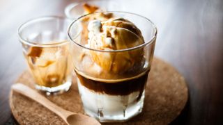An affogato in a glass on a cork board with a wooden spoon