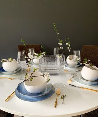 Elegant Easter dining table styling with cracked egg shape bowls, cherry blossom twigs, and blue and gold accents.