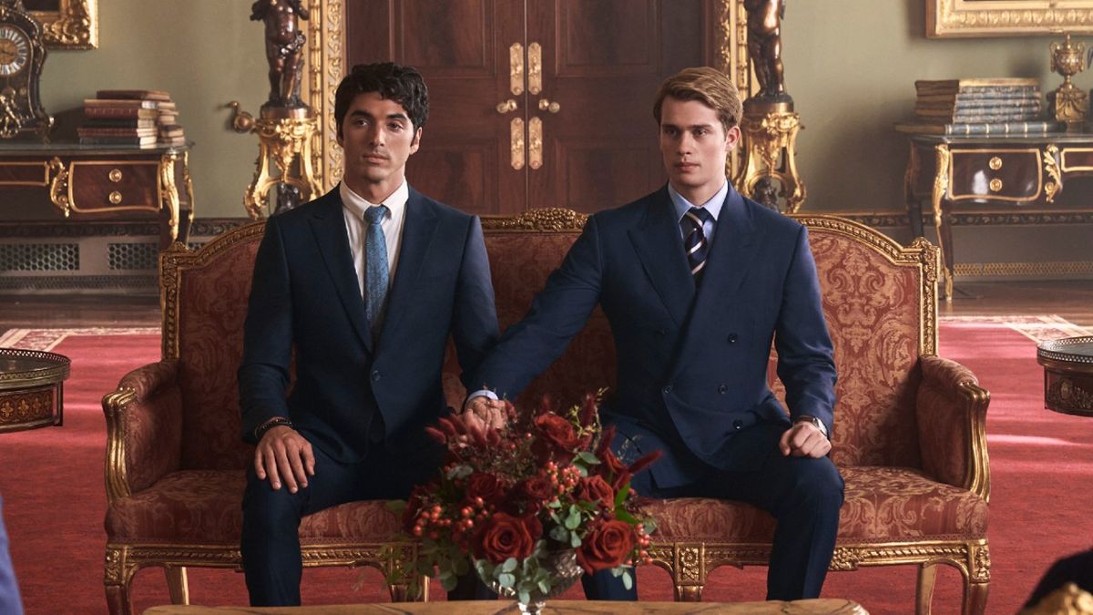 Alex and Henry sitting together holding hands looking during a meeting with the King of England.