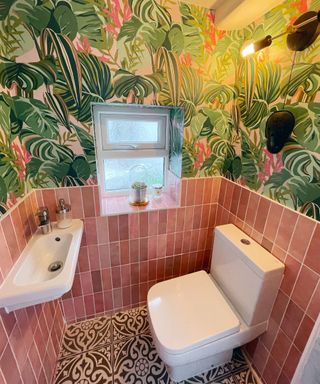 Pink tiled cloakroom downstairs toilet with palm printed wallpaper and mosaic tiles