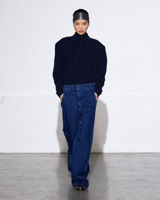 Model wearing navy blue turtleneck sweater and baggy jeans on Tibi Fall/Winter 2024 runway.