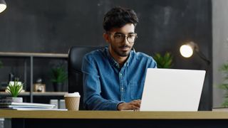 a man at his desk on a laptop next to a coffee cup