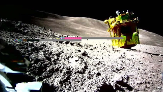 A yellow-colored spacecraft is upside down on the moon. There's a digital artifact in the center of the image.