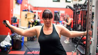 Woman using cable machine to perform lateral raise shoulder exercise