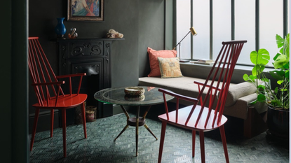 A dark gray living room with a black fireplace, red chairs, a glass coffee table, and a beige daybed
