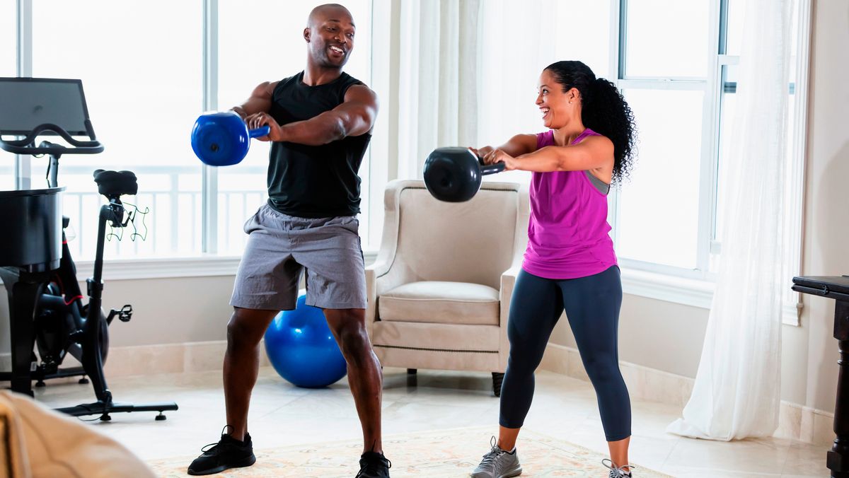 Man and woman perform kettlebell swing exercise in living room