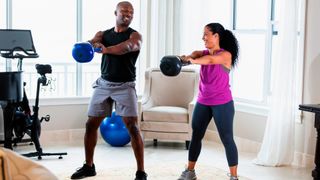 Man and woman perform kettlebell swing exercise in living room