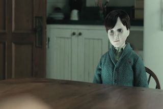 a boy doll in a sweat sitting at a table in 'The Boy'