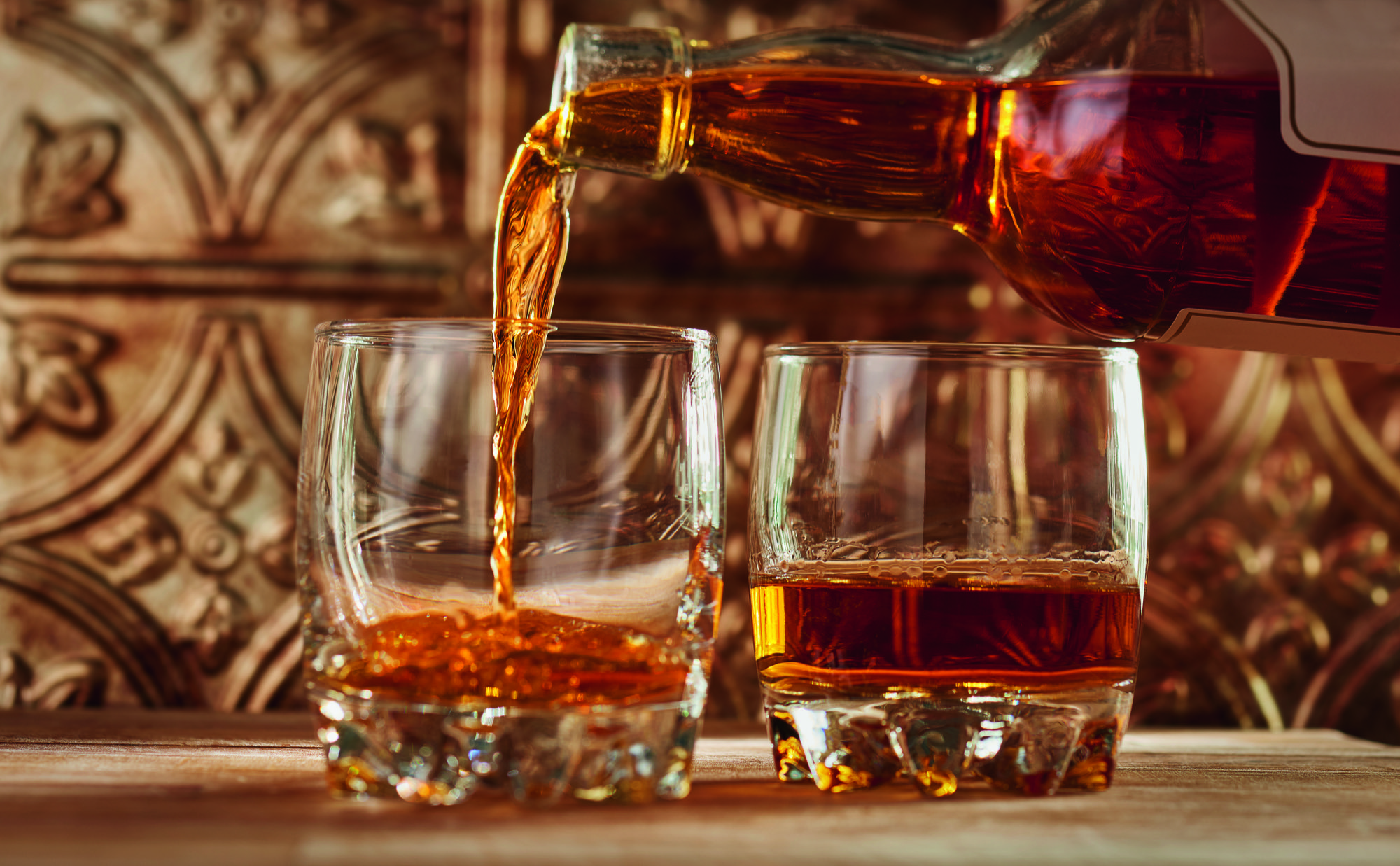 Two glasses being filled with whisky from a bottle