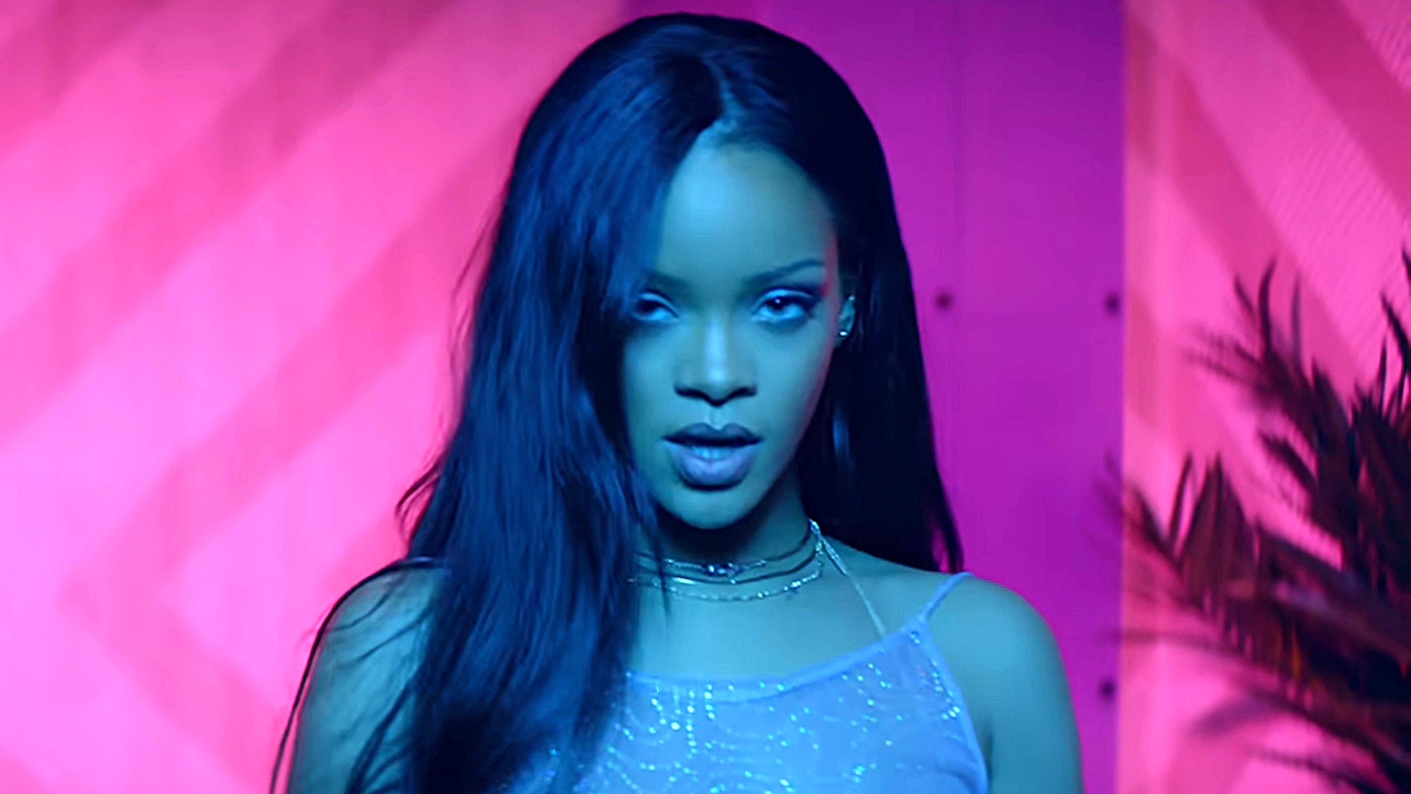 Rihanna is shown in blue light against a hot pink background wearing a glittery pink top in her music video for Work.