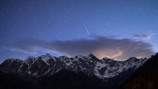 A meteor streaks through the sky above a snow-capped mountain. 