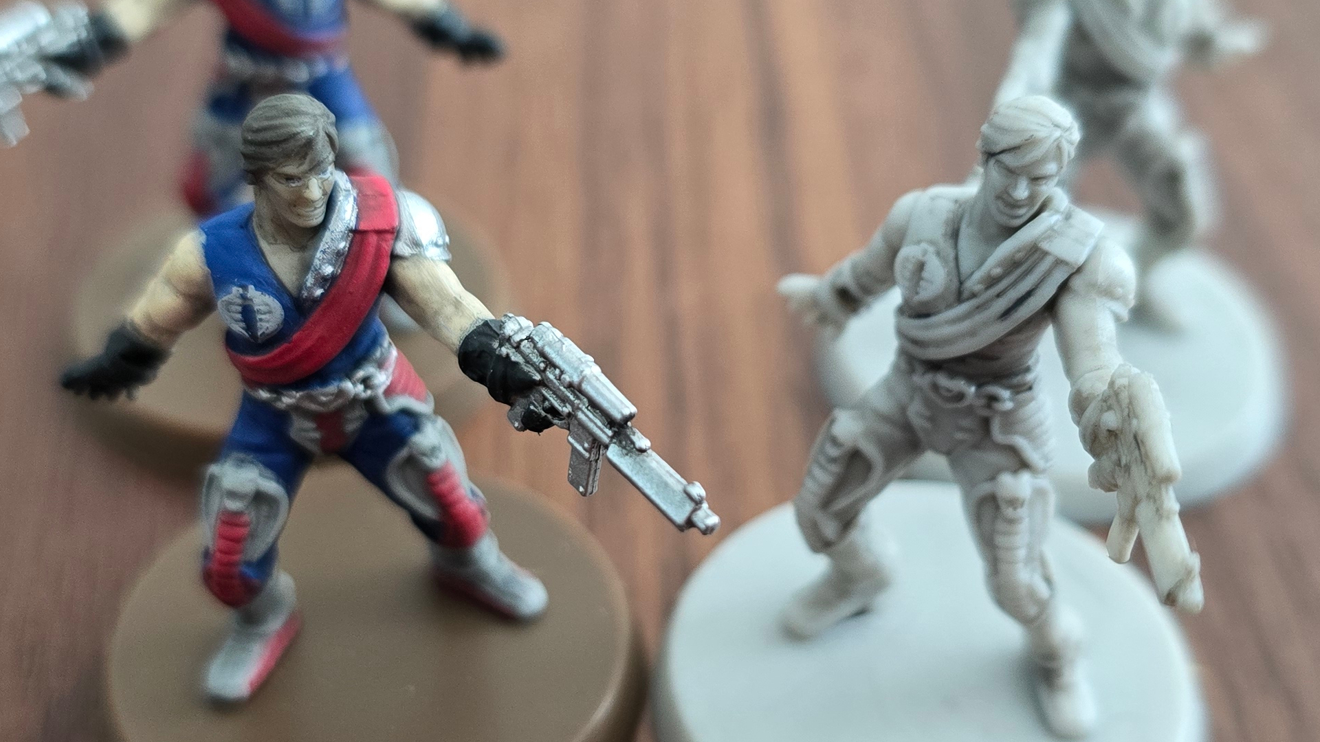 Two G.I. JOE models, some painted and some night, beside each other on a wooden surface