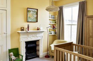 yellow gender neutral nursery, bookshelf, green chair, wooden cot and wardrobe