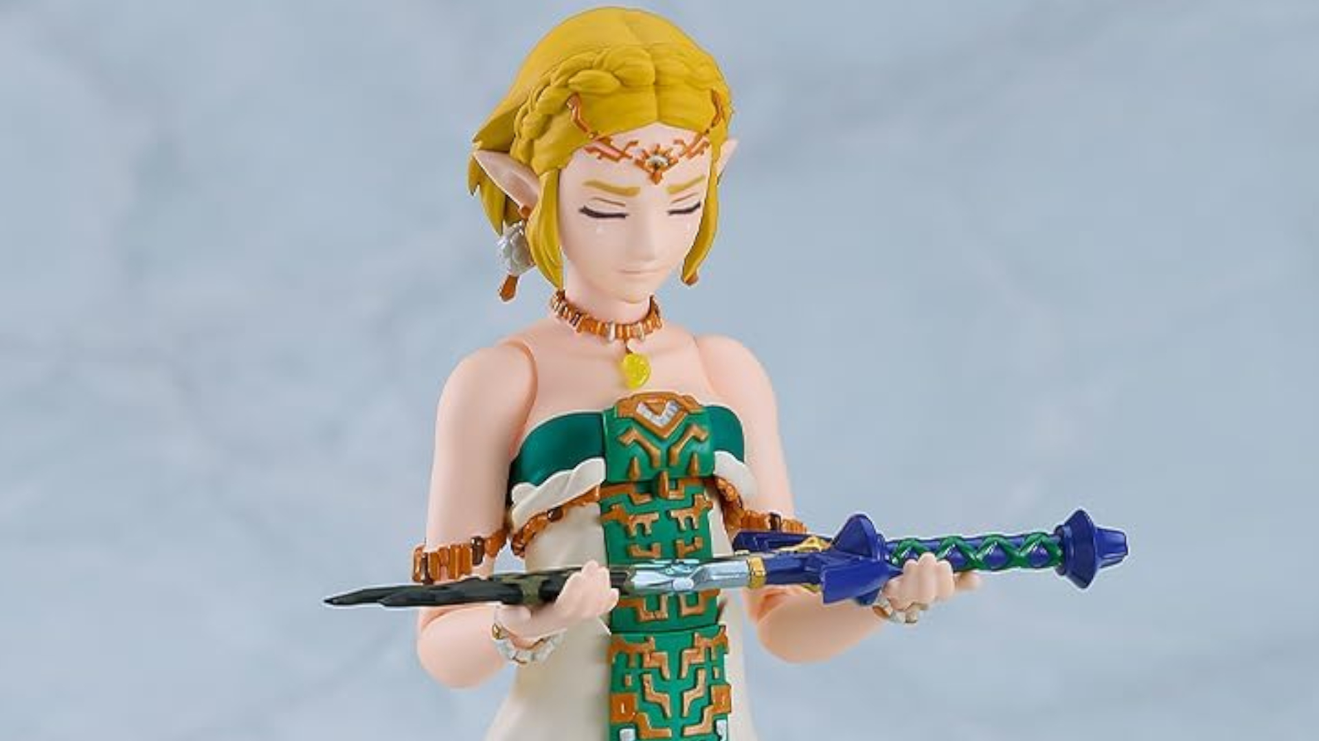 Zelda figma toy holds out the broken Master Sword against a gray background