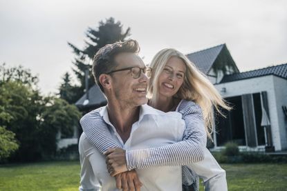 Happy couple embracing in the garden of their country house. They have a high net worth.