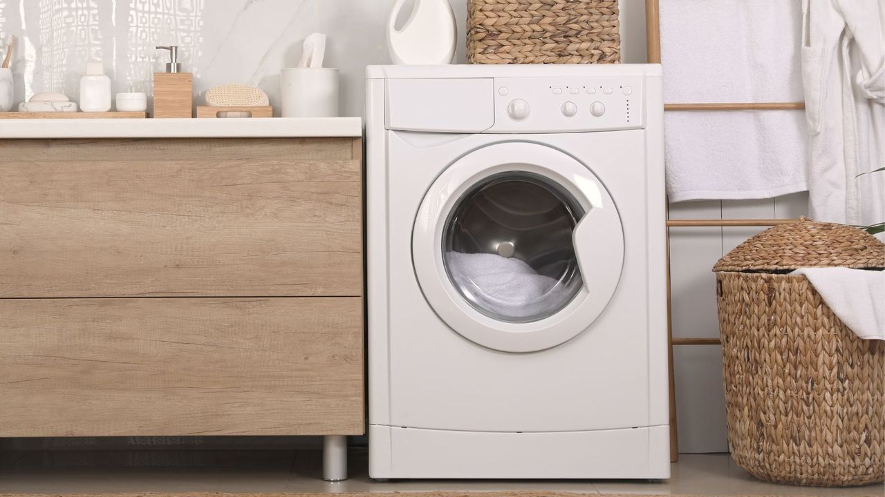 A washing machine fitted next to wooden cabinets on the left with a washing basket on the right