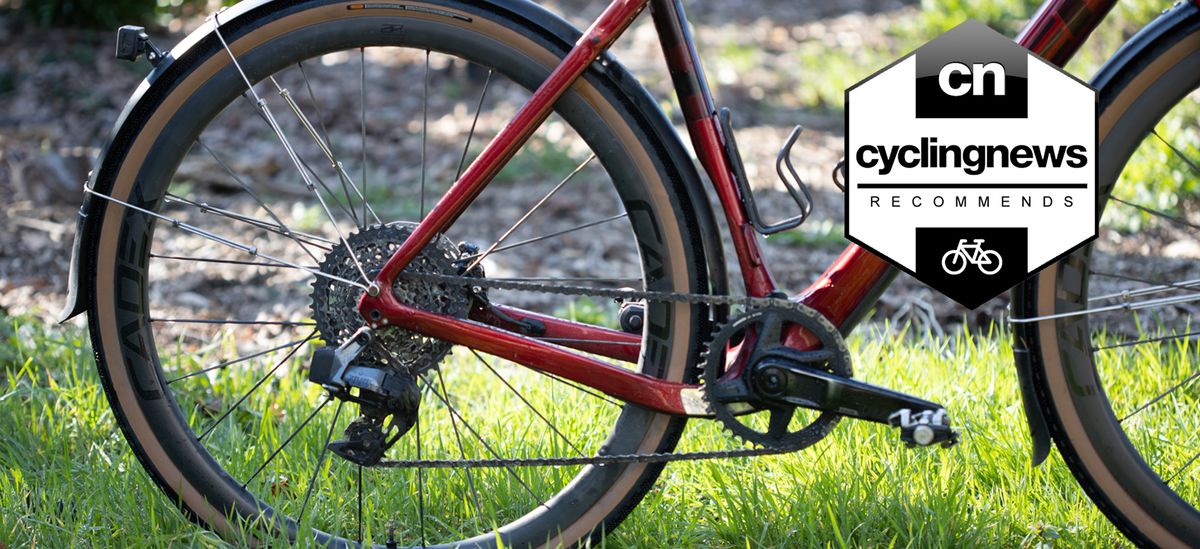 The rear end of a red bike stood on some grass in front of a stone wall