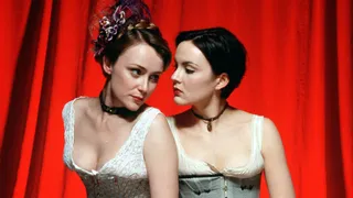 two women dressed in corsets on stage in front of a red curtain in tipping the velvet