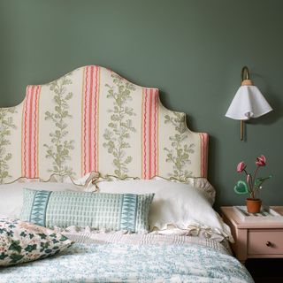 Green bedroom with patterned upholstered headboard and decorative wall light