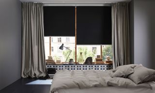 Blackout blinds with gray drapes in bedroom with houseplants and dark bedding