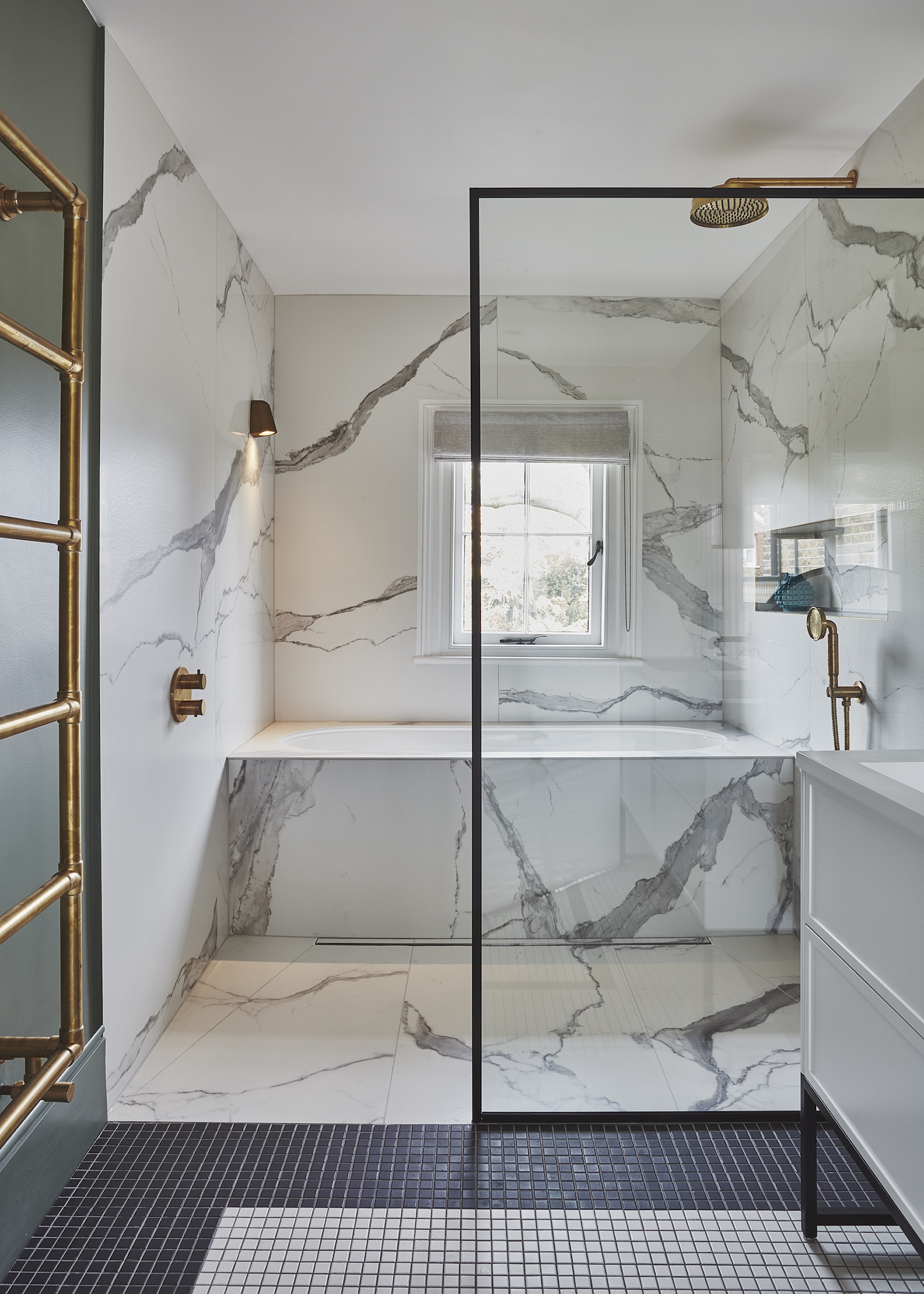 a compact bathroom showing an ergonomic layout with built in bath, walk in shower and vanity unit. A mix of marble tiling and black and white mosaics