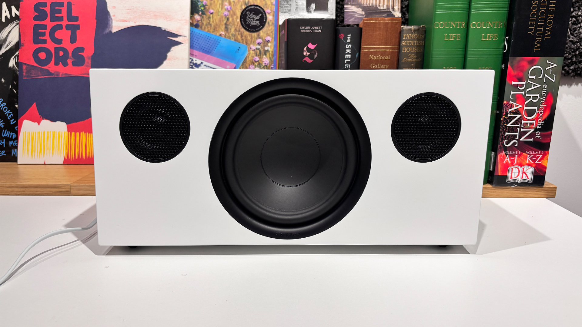 Audio Pro C20 W wireless speaker on white surface in front of busy bookcase