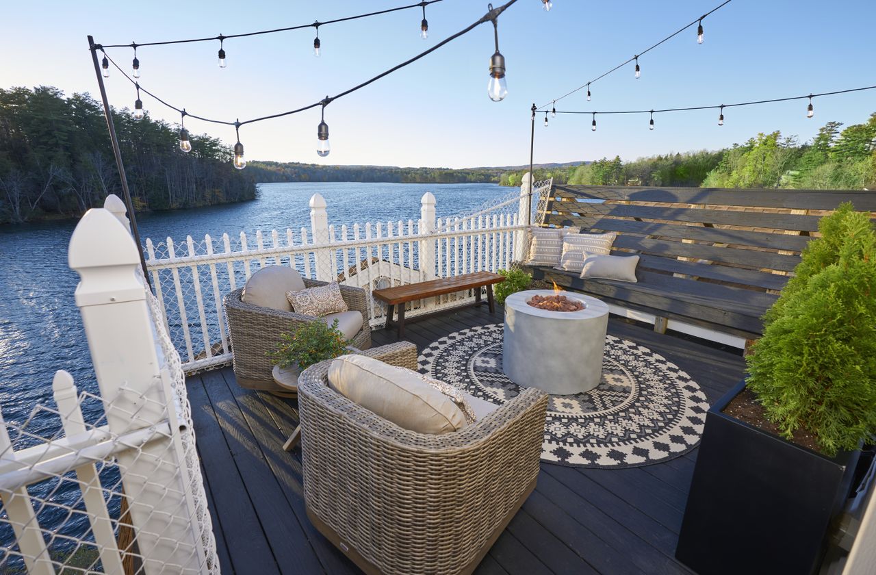 A boho style rooftop deck with rugs, seating and string lighting