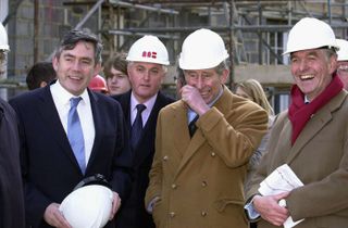 King Charles laughs while wearing a construction helmet during a visit to the Dorset village of Poundbury on February 16, 2005