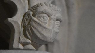 A carved face wearing a mask commemorates the restoration project taking place during the COVID-19 pandemic. 