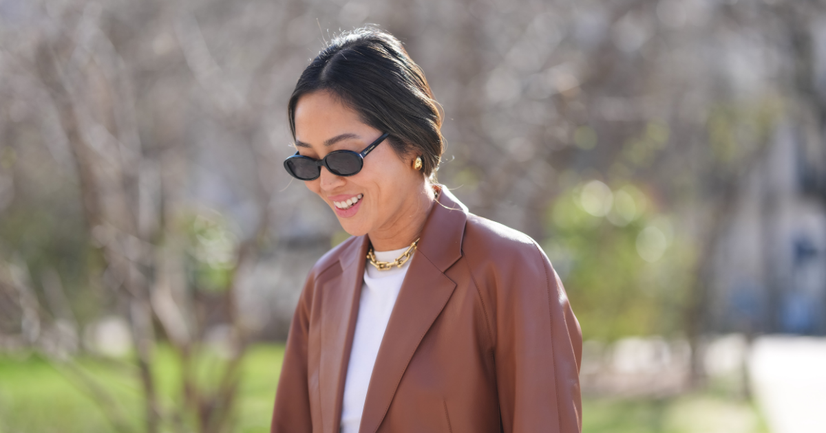 Korean SPF K-Beauty SPF Aimee Song wears black sunglasses, gold earrings, white t-shirt, shiny dark brown leather blazer jacket, outside Hermès, during the Paris Fashion week