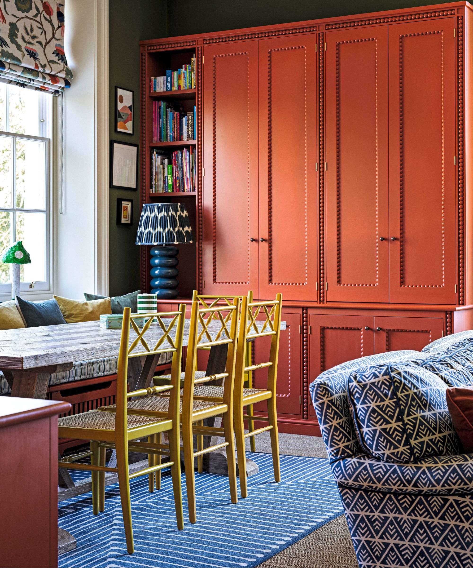 a dark green painted playroom with red cabinetry and a banquette seat with yellow dining chairs