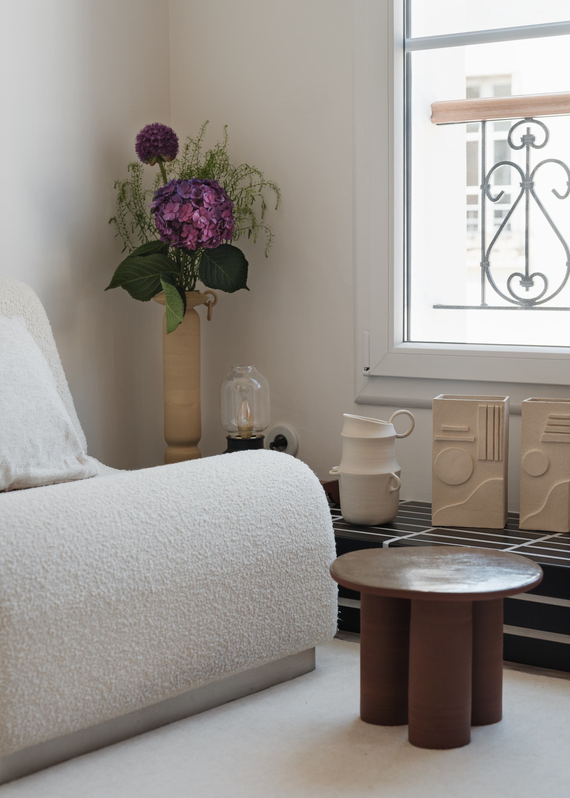 sitting area in parisian apartment with white boucle sofa, purple floral arrangement and ceramic displays