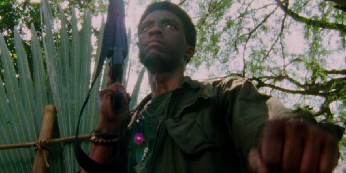 Da 5 Bloods Chadwick Boseman walking armed through the jungle