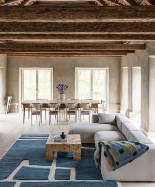 rustic barn with ceiling beams and modern living room set up with a large blue rug