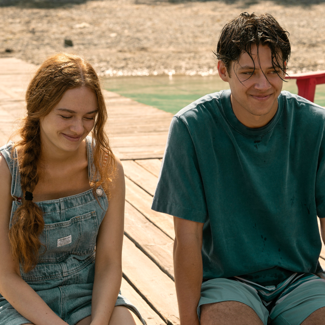 Two teenagers (Sadie Soverall as Percy Fraser, Matt Cornett as Sam Florek) sitting on a a wooden dock over a lake, in 'Every Year After.'