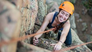 A woman rock climbing in an orange helmet