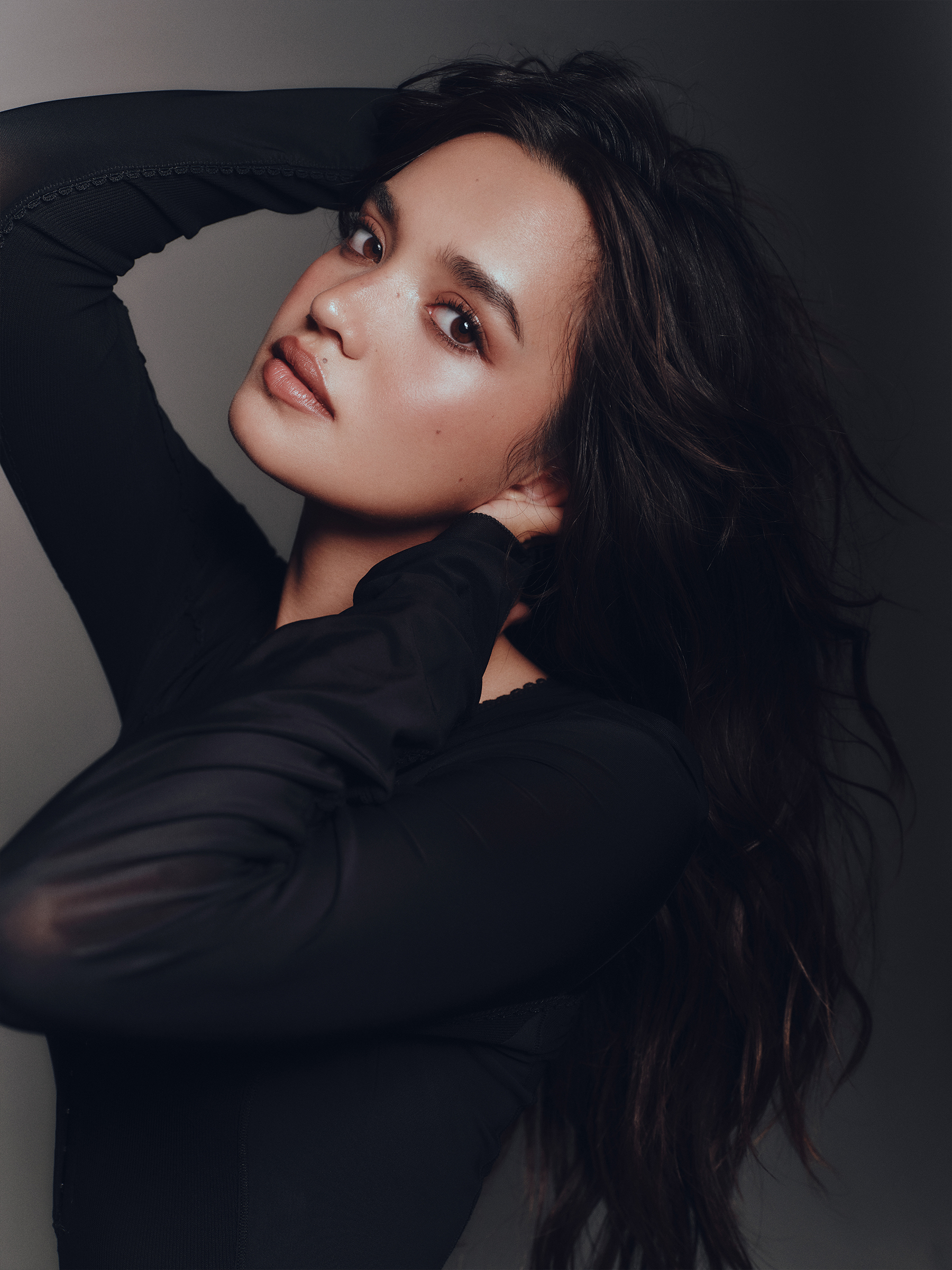 Sophia Hammons poses with her hands up in her hair. She is wearing a long-sleeve black dress.
