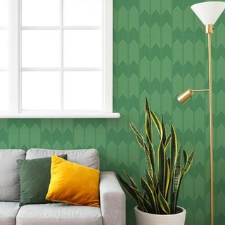 Bright green chevron wallpaper on a wall with a window by the side and a grey sofa and gold lamp in front of it