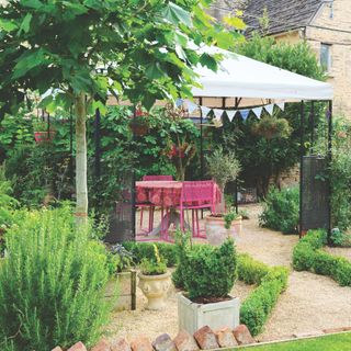 Gravel garden with lots of green plants and a fabric pergola in the middle of it