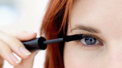 red haired female applying mascara