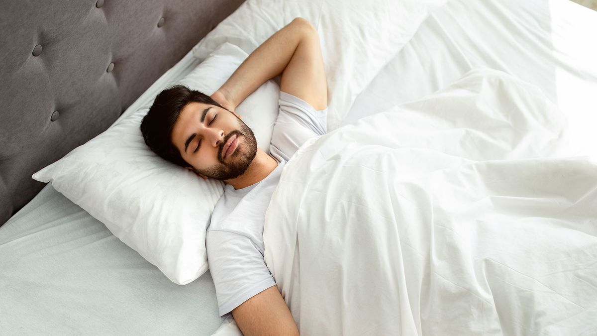 A man lies on his back in bed, sleeping happily in a comfortable position