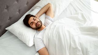 A man lies on his back in bed, sleeping happily in a comfortable position