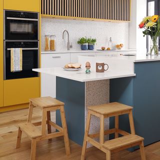yellow kitchen wall with island unit and drop surface with wooden stools